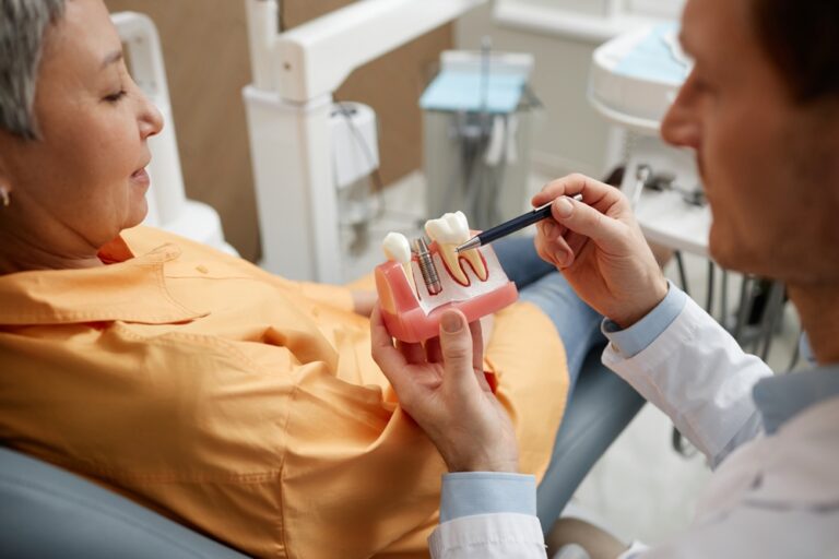 Male dentist holding tooth model while explaining dental implant surgery