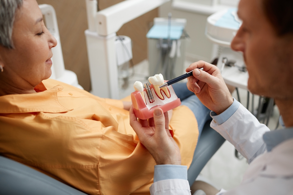 Male dentist holding tooth model while explaining dental implant surgery