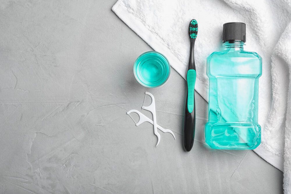 Mouthwash and other oral hygiene products on colored table